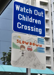 Student traffic safety artwork displayed beneath a children crossing sign.